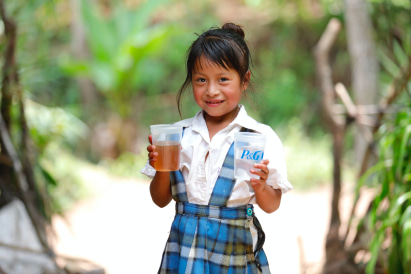 little southeast asian girl holding 2 P&G branded plastic cups, 1 of tea and 1 of water.