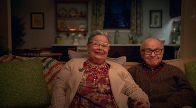 photo of an elderly couple sitting on a green couch smiling
